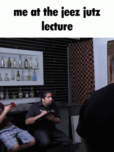 Man Sitting Before Shelf of Bottles Saying Me at the Jeez Jutz Lecture