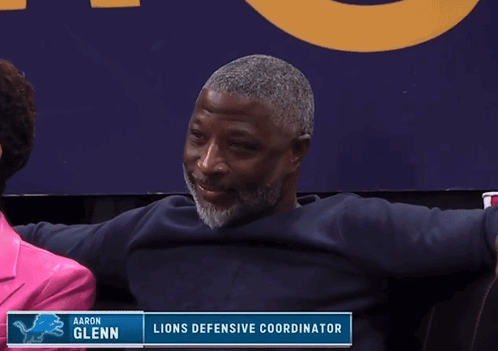 Man Sitting by Aaron Glenn Lions Defensive Coordinator Sign