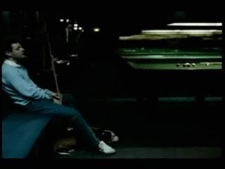 Man Sitting by Pool Table with Cue