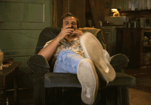 Man Sitting In Chair Feet Up Eating Hamburger GIF