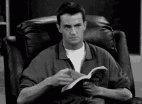 Man Sitting In Chair Reading Book Making Funny Face GIF