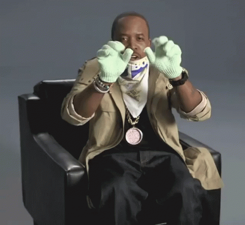 Man Sitting in Chair Wearing Green Gloves and Bo Pendant