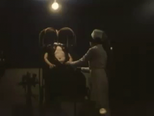 Man Sitting In Chair With Nurse In Dark Room GIF