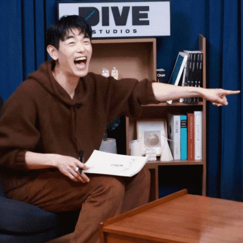 Man Sitting In Front Of Dive Studios Sign GIF