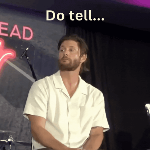 Man Sitting in Front of Do Tell Neon Sign