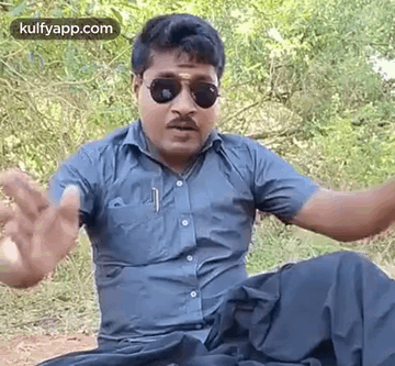 Man Sitting in Woods With Sunglasses and Blue Shirt