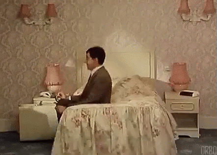 Man Sitting on Bed in Hotel Room Talking on Cell Phone