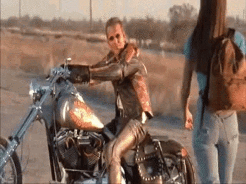 Man Sitting on Motorcycle in Desert, Woman Behind