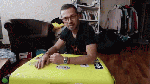 Man Sitting on Yellow Suitcase with A Sticker