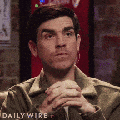 Man Sitting With Hands Folded in Front of Daily Wire Sign