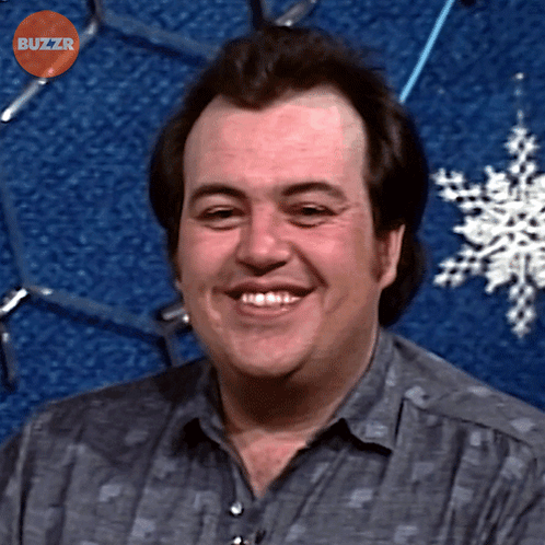 Man Smiling In Front Of Blue Background With Buzzr Text GIF