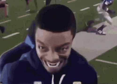 Man Smiling on Football Field With Player Running Behind