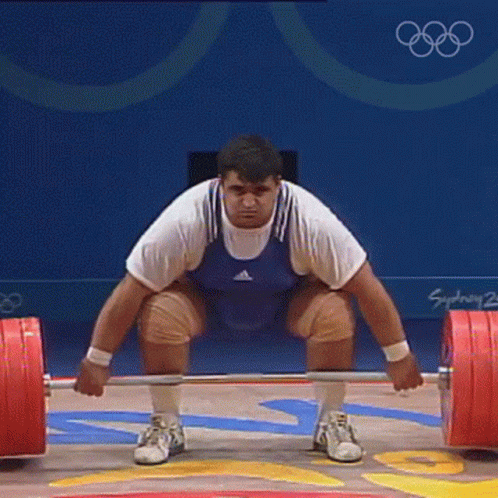 Man Squatting With Barbell in Front of Sydney 2002 Sign