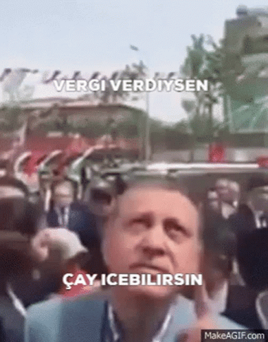 Man Standing Before Crowd With Vergi Verdiysen Sign