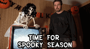 Man Standing Beside Skeleton in Front of TV Saying Time for Spooky Season