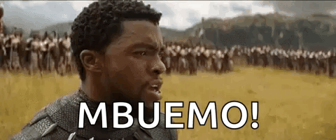 Man Standing in Field With Crowd Saying Mboemo