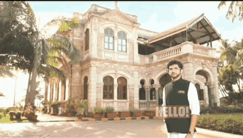 Man Standing In Front Of Building Saying Hello GIF