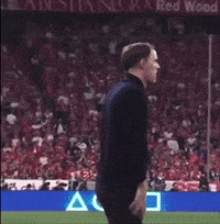Man Standing on Soccer Field in Front of Red Wood Sign
