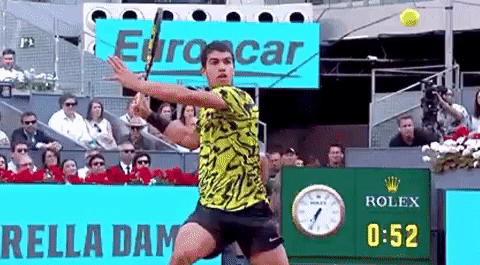 Man Swinging Tennis Racket at Ball In Front of Rolex Sign