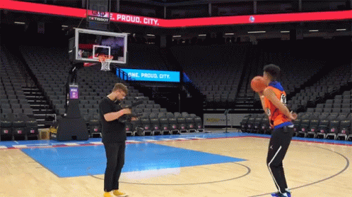 Man Taking Picture of Basketball Player on Court With Proud City Sign