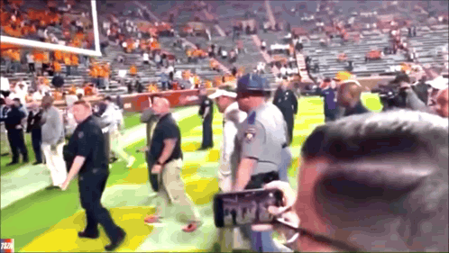 Man Taking Picture Of Police Officer On Football Field GIF