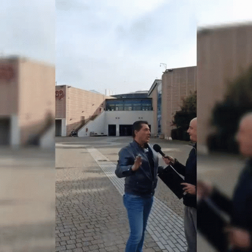 Man Talking Into Microphone in Front of Building With PP