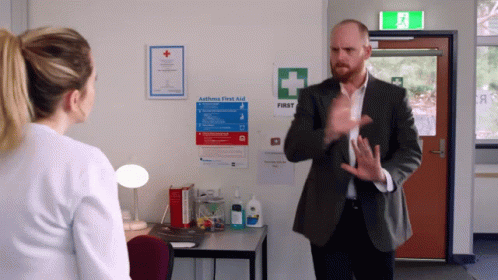 Man Talking to Woman in Front of First Aid Sign