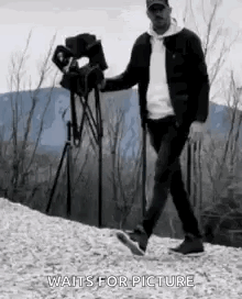 Man Walking Down Hill Holding Camera and Tripod