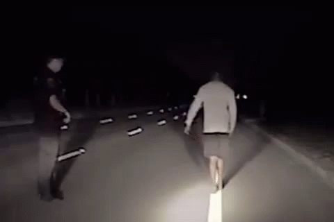Man Walking Down Road at Night With Police Officer Behind