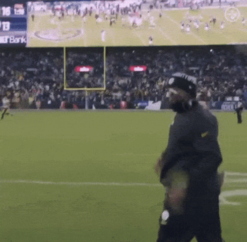 Man Walking on Football Field With Bank Screen