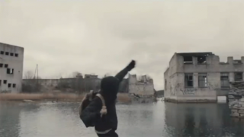 Man with Backpack Jumping Over Water by Graffiti Building