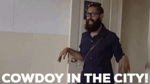 Man With Beard and Glasses Standing in Front of Cowdoy Door