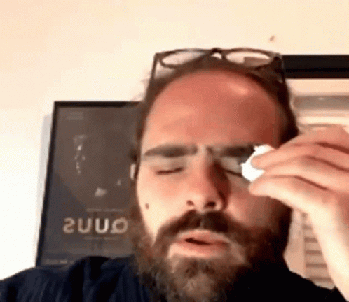 Man With Beard and Glasses Wipes Eye With Napkin