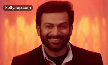 Man With Beard and Suit Smiling in Front of Red Background