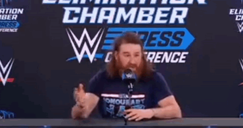 Man With Beard at Table With Microphone Chamber Sign