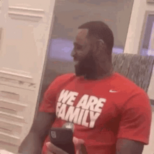 Man With Beard in Red Shirt Saying We Are Family Holding Cell Phone