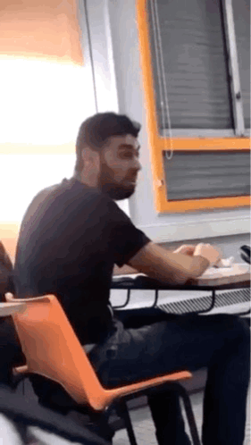 Man With Beard Sitting At Table In Classroom GIF