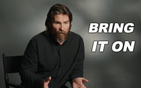 Man With Beard Sitting In Front Of Bring It On Sign GIF