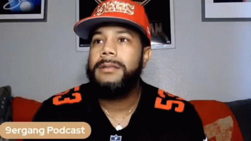 Man With Beard Sitting on Couch in Hat and Jersey