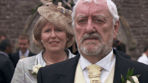 Man With Beard Standing Next To Woman In Hat GIF