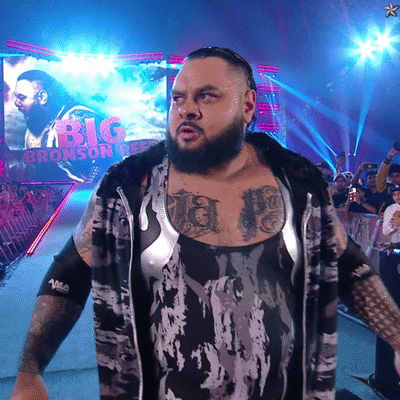 Man With Chest Tattoo In Front Of Big Bronson Banner GIF