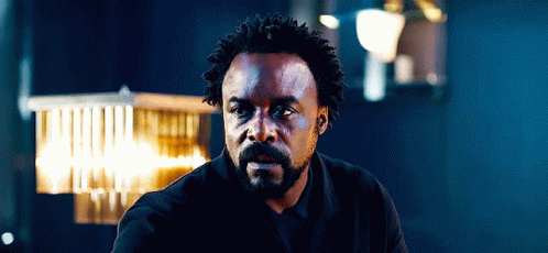Man With Curly Hair And Beard Sitting In Dark Room GIF