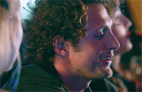 Man With Curly Hair Smiling in Dark Room