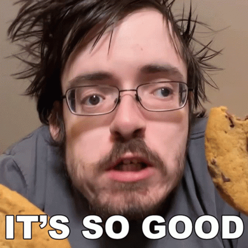 Man With Glasses and Beard Holding Cookie Saying It's So Good