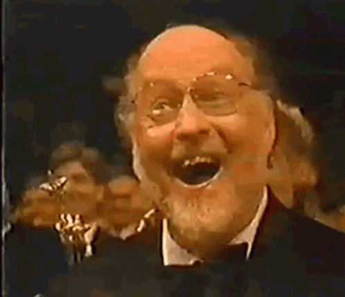 Man With Glasses and Beard Laughing Before Crowd