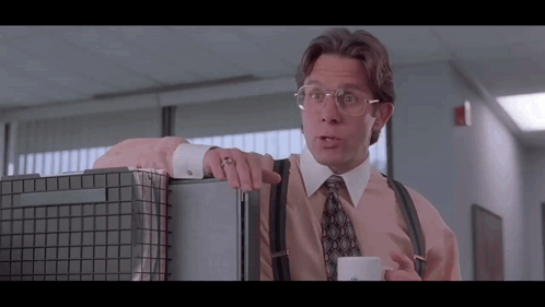 Man With Glasses and Suspenders Leaning on Cubicle With Coffee