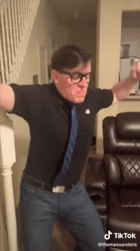 Man With Glasses and Tie Dancing in Front of Couch and Stairs