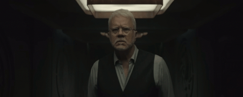 Man With Glasses and Vest Standing in Dark Room