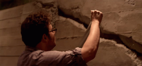 Man With Glasses Holding Fist Up Against Wall GIF