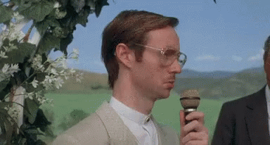 Man With Glasses Holding Microphone in Green Field